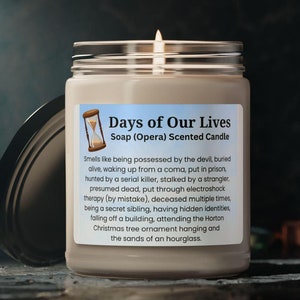 May include: A brown glass candle jar with a white label that reads "Days of Our Lives Soap (Opera) Scented Candle". The label also includes a small hourglass graphic and a description of the scent, which is inspired by the popular soap opera.