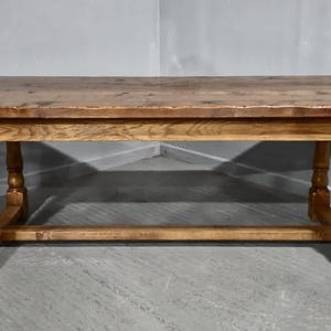 May include: A rectangular wooden table with a light brown finish. The table has four turned legs and a stretcher bar connecting the legs. The tabletop is a darker shade of brown. The table is approximately 183 cm long.