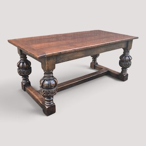 May include: A rectangular wooden table with a dark brown finish and a smooth top surface. The table features four thick, carved legs with prominent bulbous, decorative detailing and a sturdy horizontal stretcher connecting the base supports.