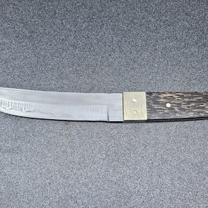 May include: A handcrafted knife with a silver blade and a dark wood handle. The blade has a curved edge and a textured surface. The handle is attached with brass hardware. The knife is designed for cutting and slicing.
