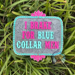 K&ouml;nnte beinhalten: Ein graues Steinschild mit einem rosa und t&uuml;rkisfarbenen Rand. Das Schild lautet "I Brake For Blue Collar Men".