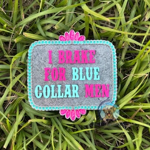 K&ouml;nnte beinhalten: Eine graue Metall-G&uuml;rtelschnalle mit t&uuml;rkisfarbenem und rosafarbenem Rand. Die Schnalle tr&auml;gt den Text "I Brake For Blue Collar Men" in rosa und t&uuml;rkisfarbener Schrift.