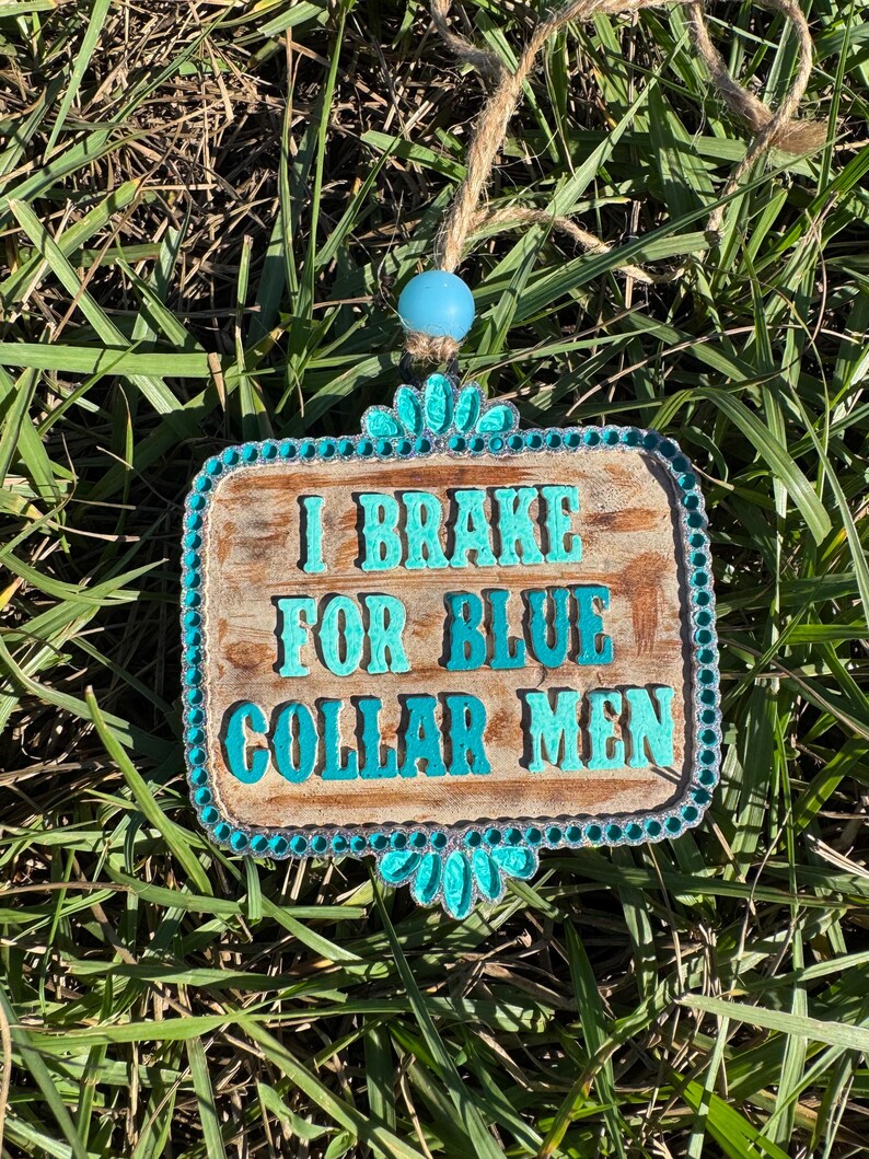 K&ouml;nnte beinhalten: Ein Holzschild mit t&uuml;rkisfarbenem Rand und Strasssteinen tr&auml;gt die Aufschrift "I Brake For Blue Collar Men".