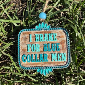 K&ouml;nnte beinhalten: Ein Holzschild mit t&uuml;rkisfarbenem Rand und Strasssteinen tr&auml;gt die Aufschrift "I Brake For Blue Collar Men".