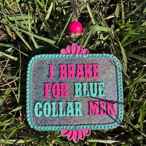 K&ouml;nnte beinhalten: Ein silbernes Glitzer-Schild mit t&uuml;rkisfarbenem Rand und rosa Blumen oben und unten. Das Schild tr&auml;gt die Aufschrift "I Brake For Blue Collar Men".
