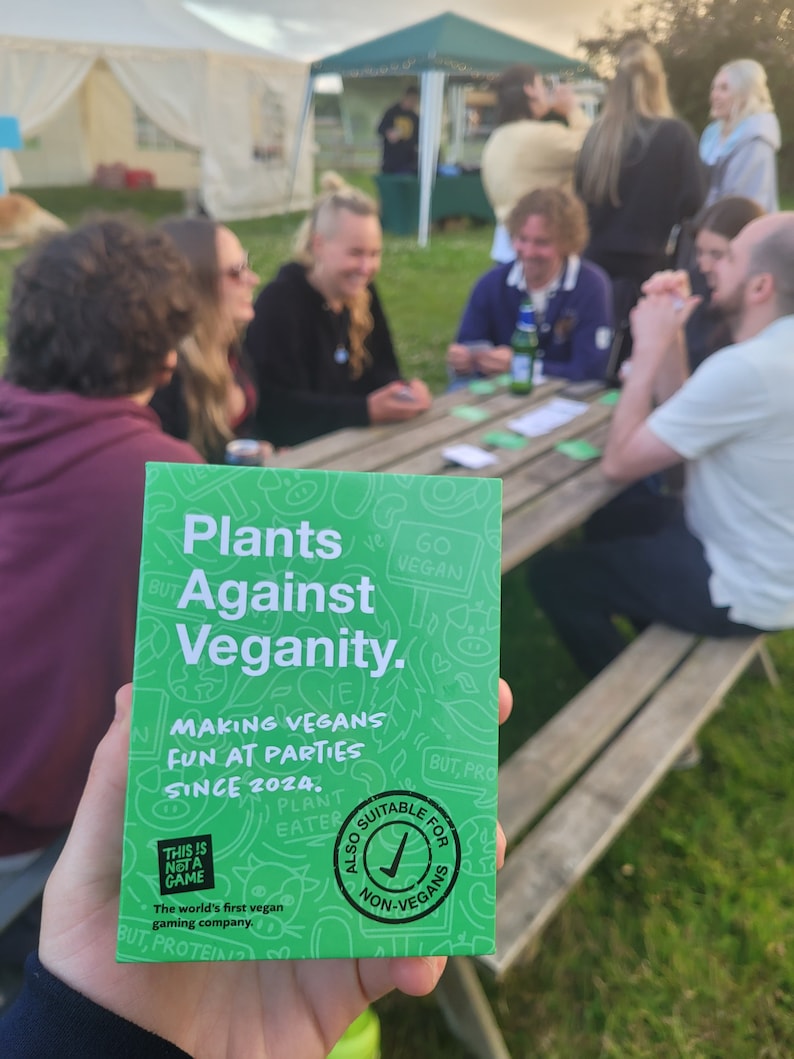 Puede incluir: Una caja de juego de cartas verde con el t&iacute;tulo "Plants Against Veganity." La caja tiene un fondo verde con texto blanco y una marca de verificaci&oacute;n en un c&iacute;rculo que dice "Tambi&eacute;n adecuado para no veganos." El texto en la caja dice "Making Vegans Fun at Parties Since 2024."