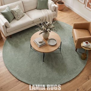 May include: A living room with a light green circular rug, a cream sofa with green cushions, and a wooden coffee table. A tan armchair and framed art pieces are also present. The rug is a key element, with the text "LAMIA RUGS" visible.