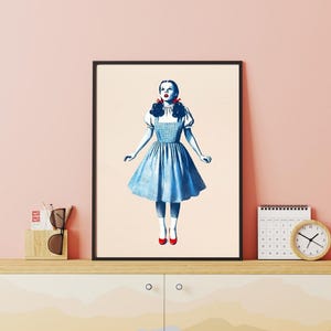 May include: A framed illustration of a woman in a blue gingham dress with red shoes, standing with her arms outstretched and looking upwards.