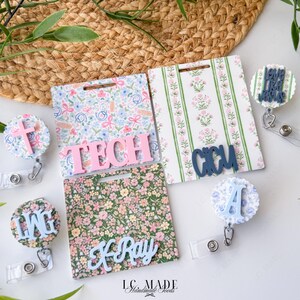 May include: A collection of floral and patterned badge reels and ID holders. The badge reels feature a cross, the letters LMG, and the words "LIVE LIKE JESUS". The ID holders have the words TECH, X-Ray, and CCU.
