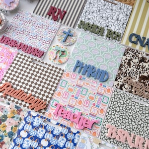 May include: A collection of square badge reels and badge holders featuring various patterns including stripes, leopard print, cow print, floral, and pumpkin designs. Each piece displays raised lettering or symbols such as RN, CNA, PHARMD, Radiology, Teacher, and BSNRN.