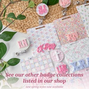 May include: A collection of floral and patterned badge reels and name tags. The tags feature pink and blue floral patterns, with pink lettering that reads "RN", "K-Ray", and "He is Risen". The image also includes the text "See our other badge collections listed in our shop".