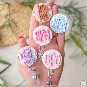 May include: A collection of five badge reels with various designs and text. The reels feature phrases like "Faith Over Fear" and "Love Like Jesus." Each reel has a unique color scheme and pattern, including floral and plaid backgrounds. The text is in a bold, readable font.