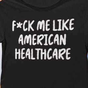 以下が含まれることがあります： 「F*ck Me Like American Healthcare」と書かれた白い文字が入った黒いクルーネックTシャツ。シャツは青い空の背景に掲げられています。テキストは太字のサンセリフ体です。