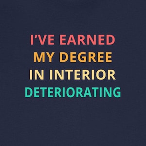 May include: A navy blue t-shirt with the text "I've earned my degree in interior deteriorating" in a rainbow color scheme.