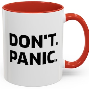 Könnte beinhalten: Weiße Keramik-Kaffeetasse mit rotem Rand und Henkel. Die Tasse trägt den Schriftzug "DON'T. PANIC." in Schwarz.