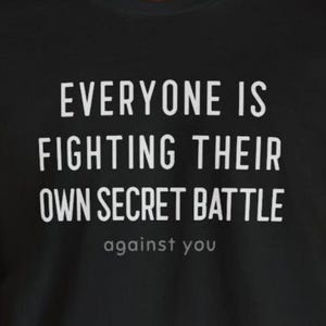 May include: Black t-shirt with white text that reads "EVERYONE IS FIGHTING THEIR OWN SECRET BATTLE" and the smaller text "against you". The shirt is a casual wear item.
