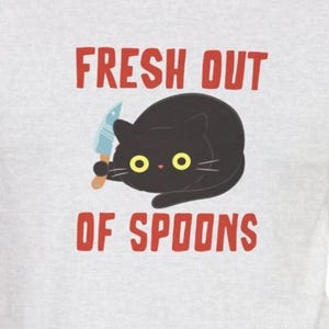 May include: A black cat with yellow eyes holding a knife, with the text "FRESH OUT OF SPOONS" in red letters on a grey t-shirt.