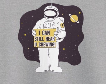 May include: A white astronaut in a space suit holding a sign that says "I can still hear u chewing!" The astronaut is in space with stars and a planet in the background.