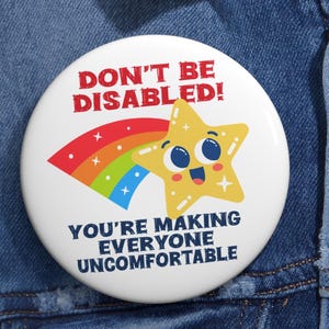 May include: A white button with the text "DON'T BE DISABLED!" in red, and "YOU'RE MAKING EVERYONE UNCOMFORTABLE" in blue. A yellow star with a rainbow arc is featured in the design.