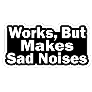 May include: A white sticker with a black rectangular background. The text "Works, But Makes Sad Noises" is printed in bold, white letters.
