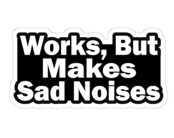 May include: A white sticker with a black rectangular background. The text "Works, But Makes Sad Noises" is printed in bold, white letters.
