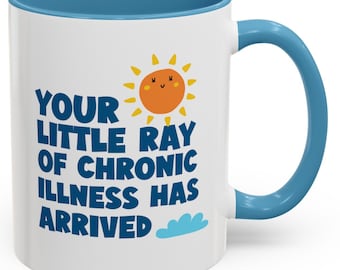 May include: White ceramic mug with a blue rim and handle. The mug features a cartoon sun with a smiling face and the text "Your little ray of chronic illness has arrived."