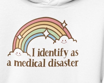May include: White hoodie with a rainbow and clouds graphic and the text "I identify as a medical disaster".