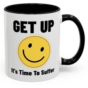 Puede incluir: Taza de café de cerámica blanca con borde y asa negros. La taza tiene una carita sonriente negra y amarilla con el texto "GET UP It's Time To Suffer" impreso en ella.