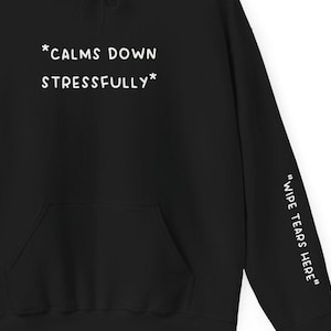 Könnte beinhalten: Schwarzer Hoodie mit weißem Text, der auf der Vorderseite "*CALMS DOWN STRESSFULLY*" und auf dem Ärmel "WIPE TEARS HERE" lautet.