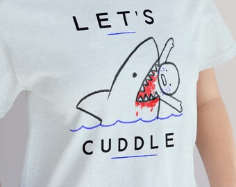 May include: A light blue t-shirt with a black and red graphic of a shark biting a person. The text "LET'S CUDDLE" is printed on the shirt.
