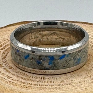 May include: A silver ring with a white and blue speckled inlay. The ring has a polished finish.