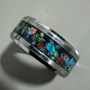 May include: A silver ring with a black band and a strip of iridescent opal embedded in the band.