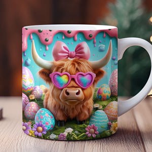 Puede incluir: Una taza de cerámica blanca con un diseño colorido que presenta una vaca de las Tierras Altas con gafas de sol rosas y un lazo. La vaca está rodeada de huevos de Pascua de colores pastel y flores.