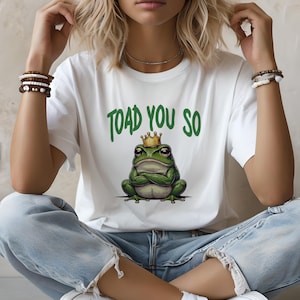 May include: White t-shirt with a green frog wearing a gold crown and the text "TOAD YOU SO" printed on it.