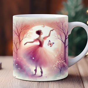 May include: White ceramic mug with a pink and purple watercolor design of a ballerina dancing in a forest with a butterfly. The mug has a white handle.