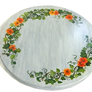 Könnte beinhalten: Eine runde, hellblaue Holztischplatte mit einem bemalten Design aus orangefarbenen Blumen und grünen Blättern am Rand.