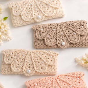 May include: Four handmade crochet clutch purses in cream, beige, and peach colours. Each purse features a scalloped flap design adorned with faux pearls. Yarn skeins and a pearl necklace are in the background.