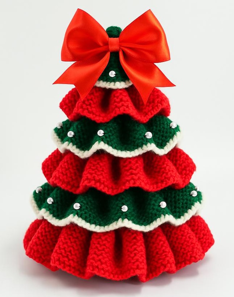 K&ouml;nnte beinhalten: Handgefertigte Weihnachtsbaumdekoration. Der Baum ist aus roter und gr&uuml;ner Wolle gestrickt, mit wei&szlig;er Bord&uuml;re und kleinen Perlen verziert. Eine gro&szlig;e rote Schleife sitzt oben auf dem Baum. Eine festliche Weihnachtsdekoration.