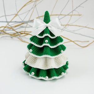 May include: A handmade, crocheted Christmas tree in green and white, adorned with faux pearls. The tree is topped with a white satin bow. The tree is a decorative item for the holiday season.