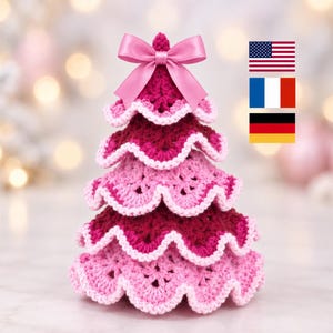 Pode incluir: Um enfeite de árvore de Natal em crochê com camadas alternadas de fio magenta escuro e rosa claro. As bordas de cada nível são finalizadas com pontos em rosa claro. Um laço de fita de cetim rosa claro está preso no topo.