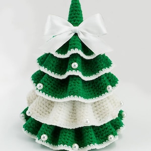 May include: A handmade, tiered Christmas tree decoration. The tree is crocheted with green and white yarn, adorned with white pearl beads and a white satin bow at the top. The tree is approximately 6 inches tall.