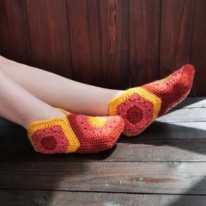 Puede incluir: Un par de zapatillas de crochet en tonos rojos, naranjas y amarillos. Las zapatillas están hechas con un patrón de panal y tienen un aspecto suave y acogedor.