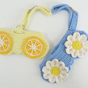 K&ouml;nnte beinhalten: Zwei geh&auml;kelte Taschen mit Handschlaufen. Eine Tasche ist hellgelb mit zwei orange-wei&szlig;en Zitrusfruchtmotiven. Die andere Tasche ist hellblau mit zwei wei&szlig;-gelben G&auml;nsebl&uuml;mchenmotiven. Beide Artikel verf&uuml;gen &uuml;ber Metallringe und Karabinerverschl&uuml;sse.