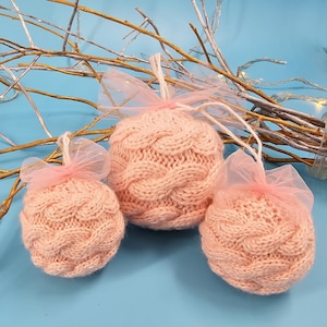 May include: Three pink knitted baubles with a cable knit pattern. The baubles are decorated with pink tulle and are perfect for adding a touch of festive cheer to your home.
