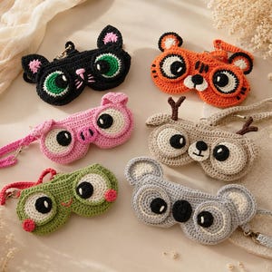 May include: A collection of six handmade crochet eyeglass cases in various animal designs. The cases feature cat, tiger, pig, deer, frog, and koala faces with large, expressive eyes. Each case has a matching strap and zipper closure, showcasing a playful and colorful aesthetic.