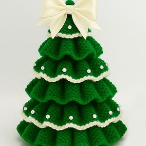 K&ouml;nnte beinhalten: Handgefertigte gr&uuml;ne Weihnachtsbaumdekoration mit wei&szlig;er Bord&uuml;re und Perlenakzenten. Der Baum ist mit einer gro&szlig;en cremefarbenen Schleife gekr&ouml;nt. Dieser festliche, geh&auml;kelte Baum ist ein bezaubernder Feiertagsakzent.
