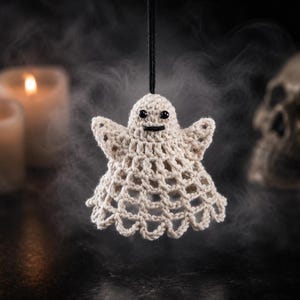 May include: A small, off-white crocheted ghost ornament featuring a bell-shaped body with an open-work lattice pattern, two small arms extended outwards, and two black bead eyes with a stitched black mouth, suspended by a thin black string.