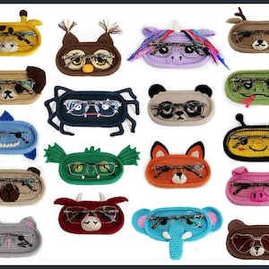 Puede incluir: Una colección de portagafas hechos a mano con ganchillo en varias formas de animales, incluyendo una jirafa, un búho, un perro, una araña, un panda, un tiburón, un dragón, un zorro, una abeja, un cerdo, un gato, un elefante y un oso. Cada soporte es de un color diferente.