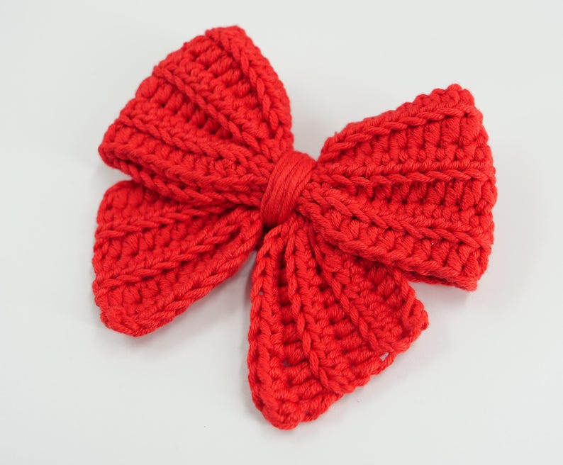 Puede incluir: Un lazo rojo brillante, tejido a ganchillo. El lazo est&aacute; hecho de hilo grueso y tiene una apariencia texturizada. Est&aacute; atado en el centro con hilo rojo a juego. Un accesorio decorativo.