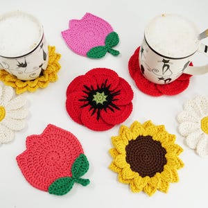 May include: A collection of handmade crochet flower coasters in various colors and designs. The coasters include daisies, sunflowers, poppies, and tulips. Two mugs with coffee and spoons rest on sunflower and red flower coasters.